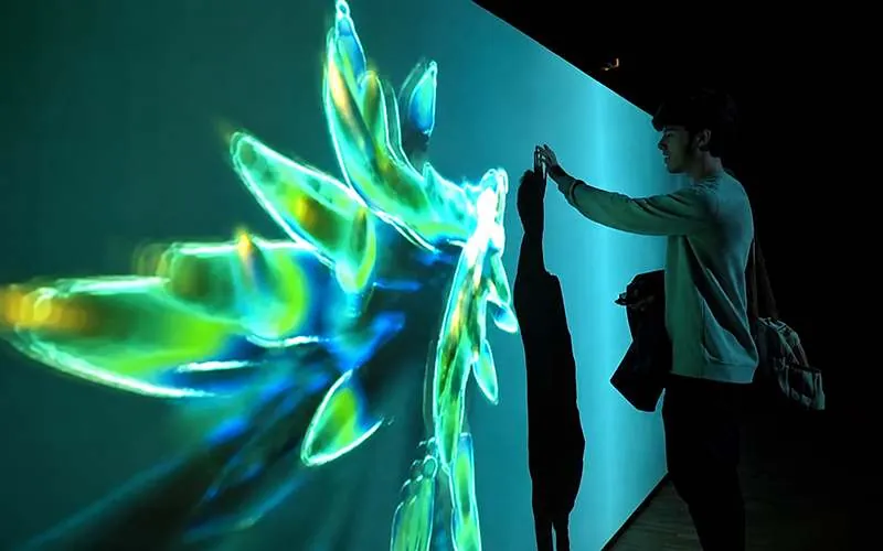 Persona tocando una proyección interactiva en un muro que reacciona a su movimiento