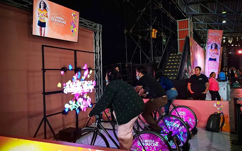 Participantes pedaleando para revelar un mensaje luminoso en un muro durante la Carrera Bonafont